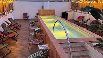 Un espace piscine aménagé sur le toit, avec des chaises longues et un petit escalier menant à la piscine.