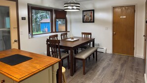 A dining area with a wooden table and chairs, a bench, a pendant light, a window with blinds, and a door with a 'No Smoking' sign. - Spacious & Comfy Family Home, minutes from the Airport! (Juneau)