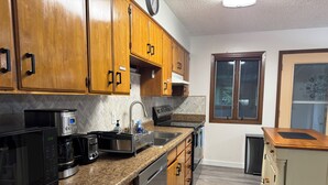 A modern kitchen with wooden cabinets, a stainless steel sink, a built-in dishwasher, and a coffee maker. - Spacious & Comfy Family Home, minutes from the Airport! (Juneau)