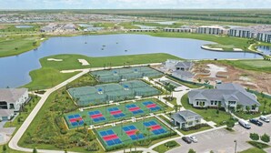 Vista aérea de un campo de golf con varias canchas de tenis, un estanque grande y edificios residenciales.