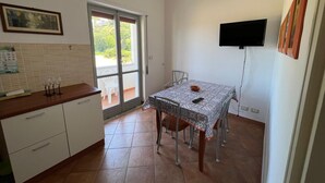 Cocina compacta con comedor, televisor montado en la pared y puerta corredera de vidrio a un espacio exterior.