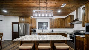 A kitchen with wooden cabinets, a granite countertop, stainless steel appliances, and a bar area with stools.
