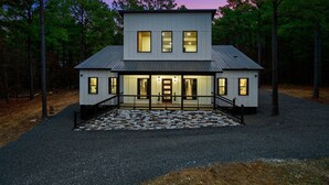 A modern two-story house with a stone-paved entrance and a metal roof, surrounded by trees.