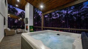 A hot tub on a wooden deck with a view of a forest at dusk.