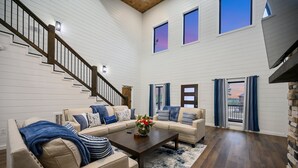 A spacious living room with a wooden staircase, a sectional sofa set, and a coffee table with a vase of flowers.