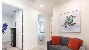A living room with a grey sofa and red cushions, a framed turtle painting on the wall, and a door leading to another room.