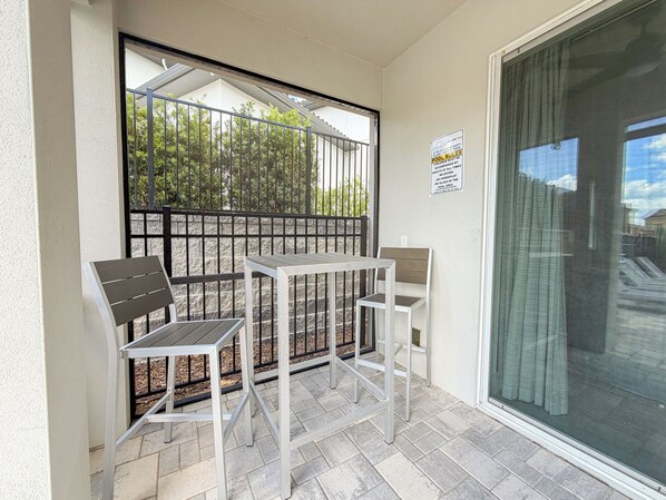 Een balkon met een tafel en stoelen, een metalen leuning en een glazen deur.