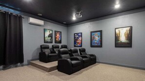 A home theater room with a carpeted floor, black leather recliners, and movie posters on the wall.