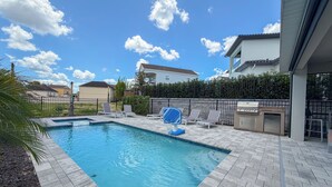 A swimming pool with a tiled deck, a barbecue grill, and lounge chairs.