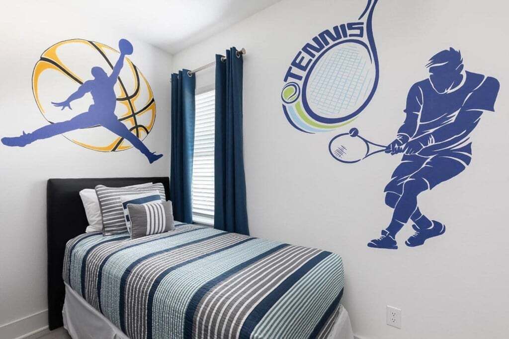 A bedroom with a bed, a window with curtains, and wall decals of a basketball player and a tennis player.