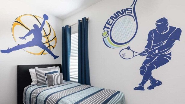 A bedroom with a bed, a window with curtains, and wall decals of a basketball player and a tennis player.