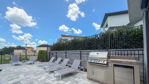 An outdoor patio with a barbecue grill, lounge chairs, and a view of the neighborhood.