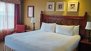 Una cama grande con cabecera de madera, una silla roja y una mesita de noche con una lámpara.