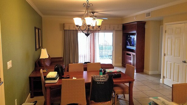 Un comedor con candelabro, sillas de mimbre, una mesa con una computadora portátil y un televisor al fondo.