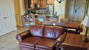 Una sala de estar con un sofá de cuero marrón, una mesa de comedor de madera y sillas de mimbre.