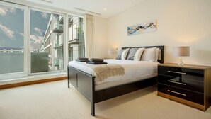 Een moderne slaapkamer met een groot bed, een nachtkastje, een lamp en uitzicht op een gebouw door grote ramen.