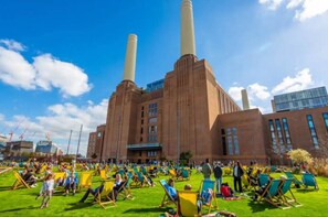 Un grand bâtiment industriel doté de deux hautes cheminées, entouré d’une zone verdoyante où se trouvent de nombreuses chaises colorées et des personnes.