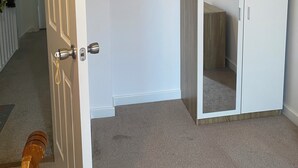 Un couloir avec une porte blanche, une armoire blanche et un tableau encadré accroché au mur.