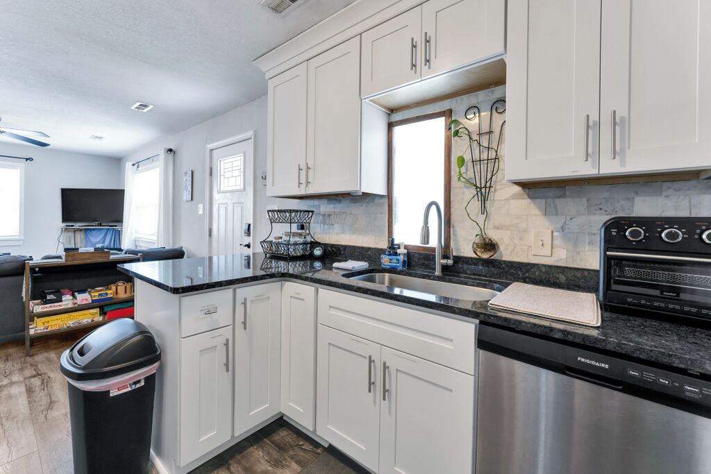 A modern kitchen with white cabinets, a black countertop, stainless steel appliances, and a window with a plant.
