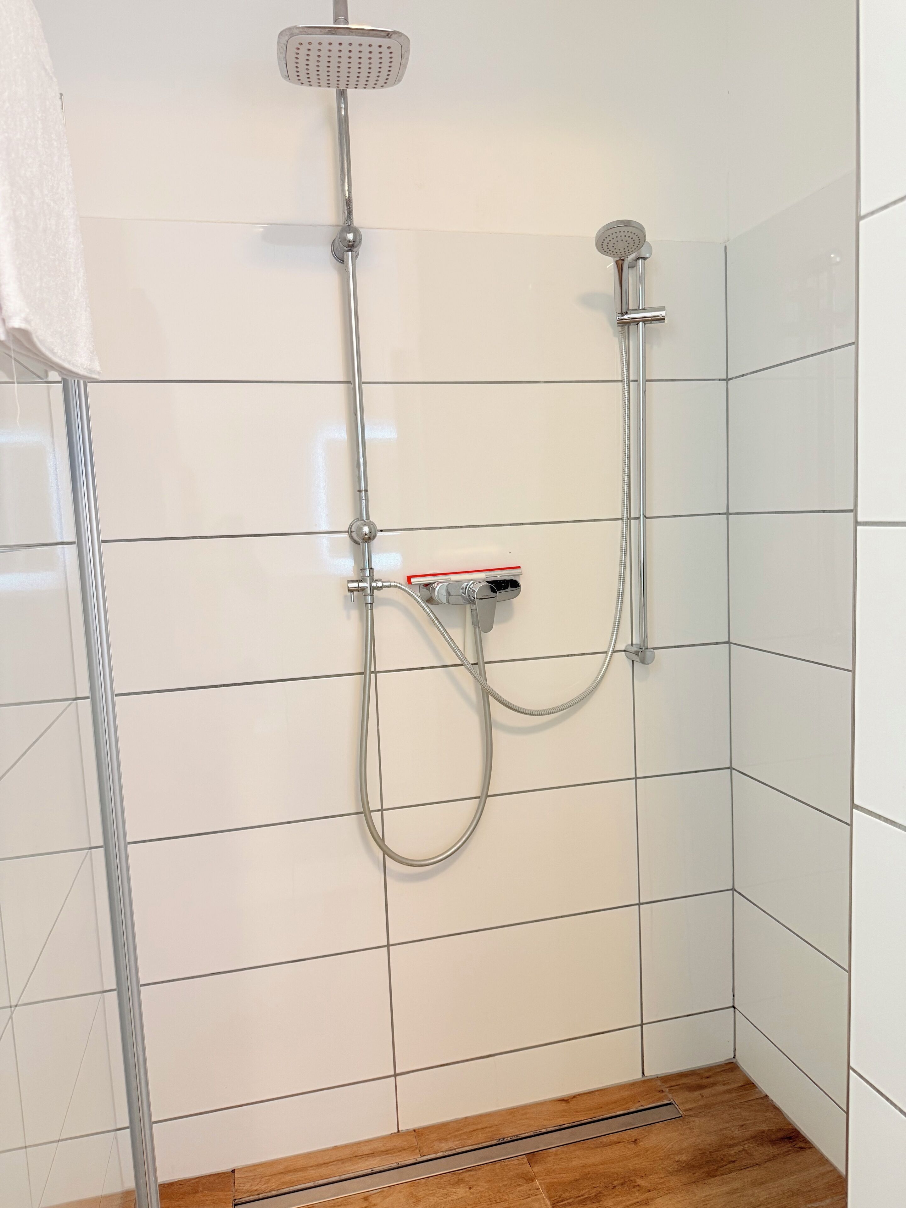 A shower with a handheld showerhead and a fixed overhead showerhead, connected to a wall-mounted control panel.