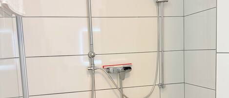 A shower with a handheld showerhead and a fixed overhead showerhead, connected to a wall-mounted control panel.