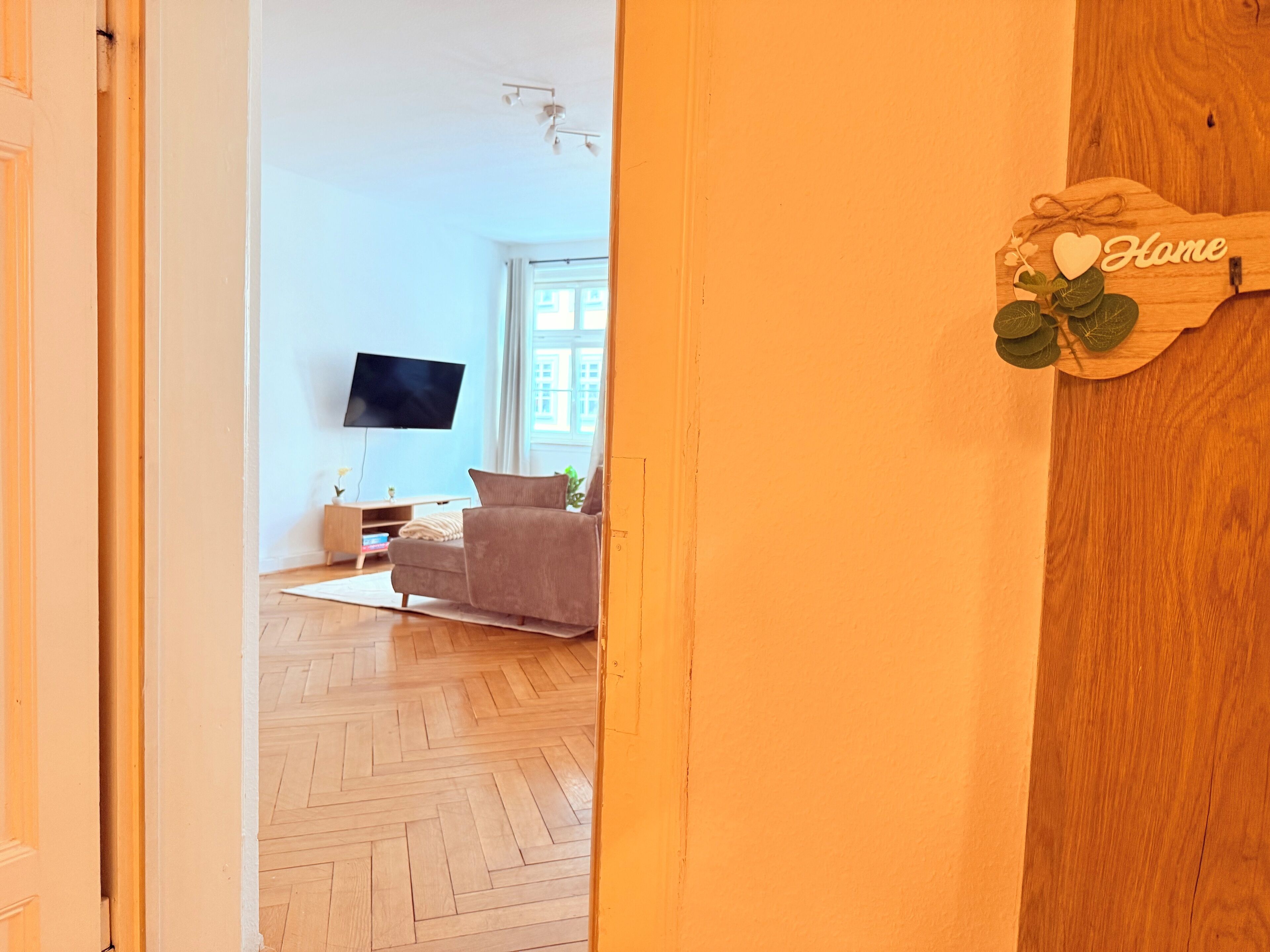 A living room with a sofa, a flat-screen TV, and a wooden sign that reads "Home".
