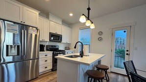 A modern kitchen with stainless steel appliances, a central island with stools, and a dining area with a bench.