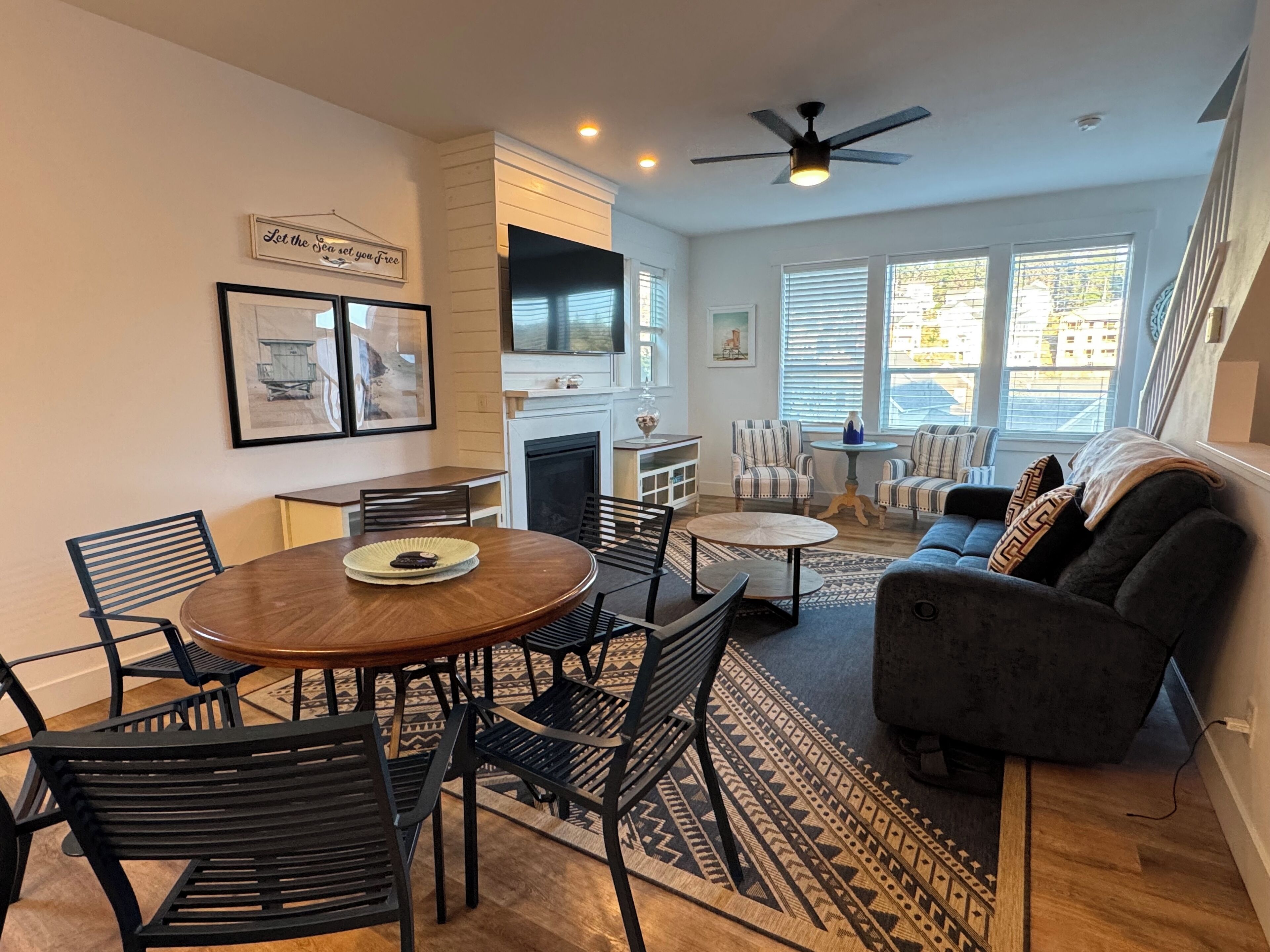 A modern living room with a fireplace, a dining area with a round table and chairs, and a sofa with patterned cushions.