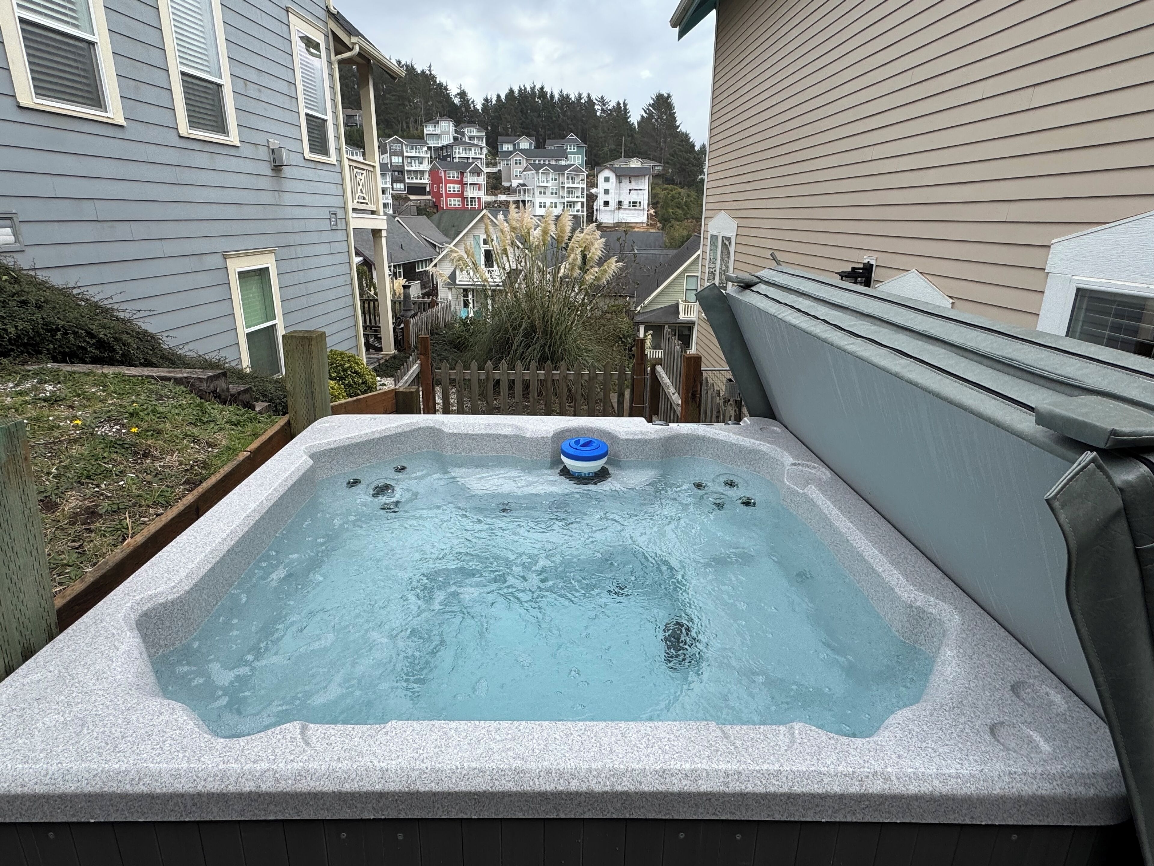 A hot tub in a backyard with a wooden fence, surrounded by houses.