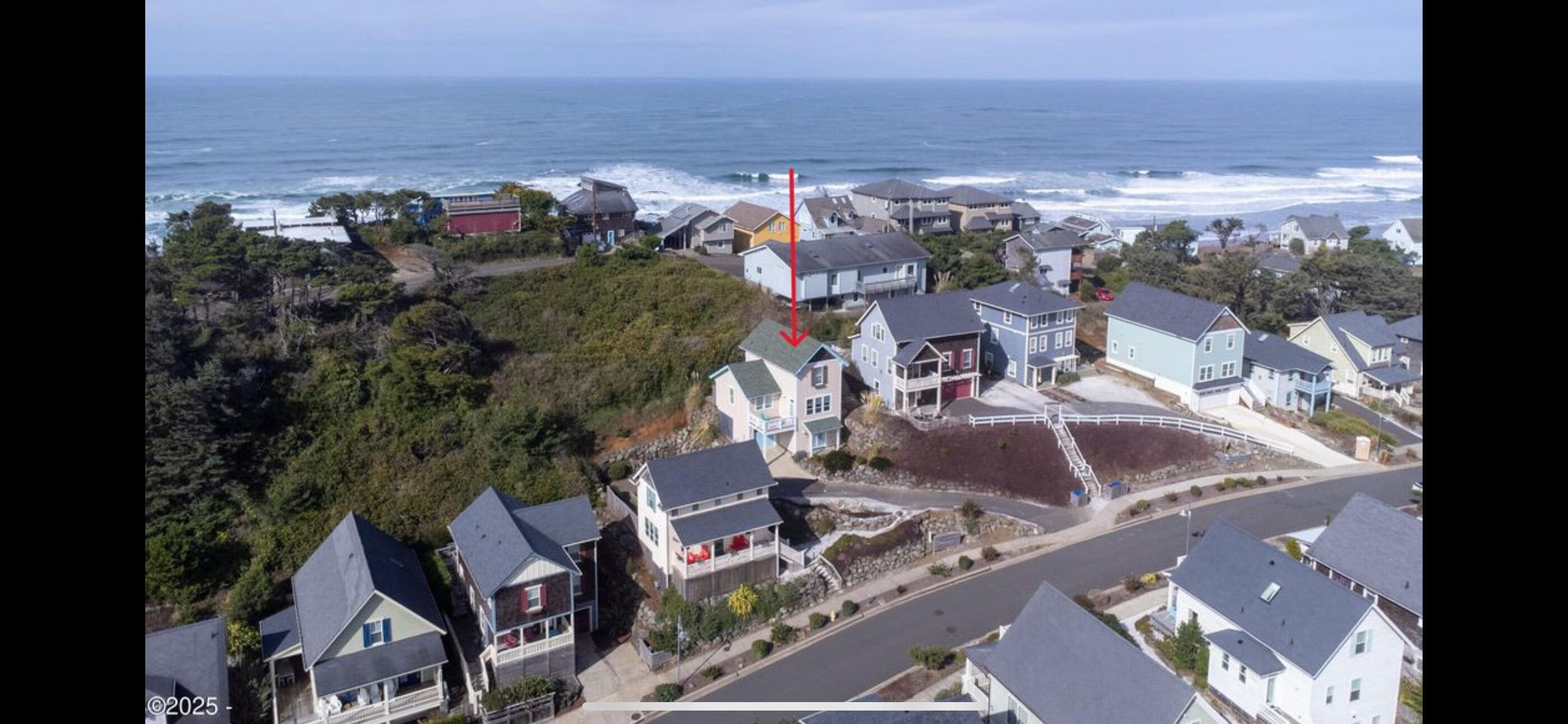 A coastal residential area with houses, a road, and the ocean in the background.