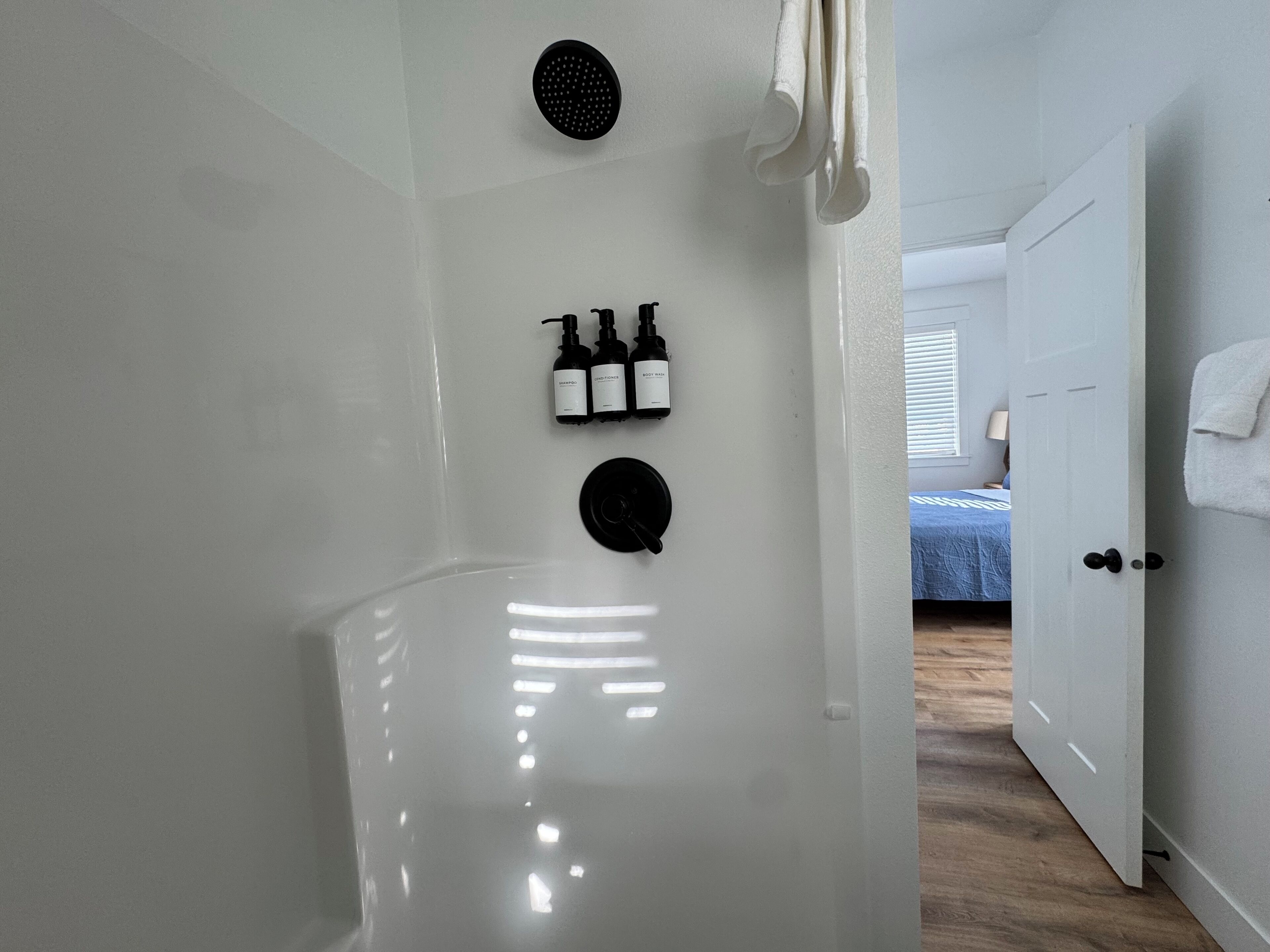 Une salle de bain avec une baignoire blanche, une pomme de douche noire et deux bouteilles de shampoing et d’après-shampoing.