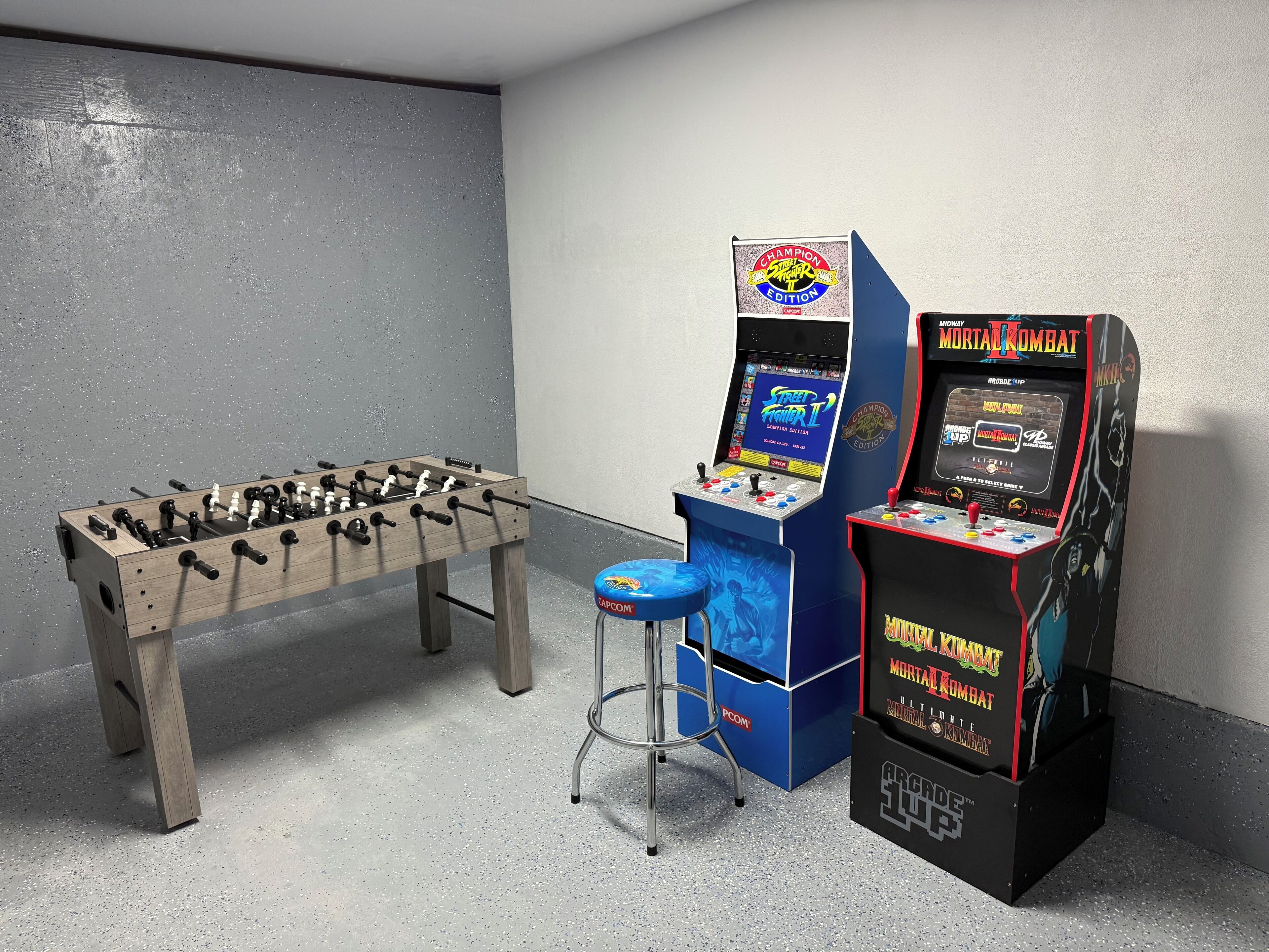 A room with a foosball table, a blue arcade machine, and a stool.