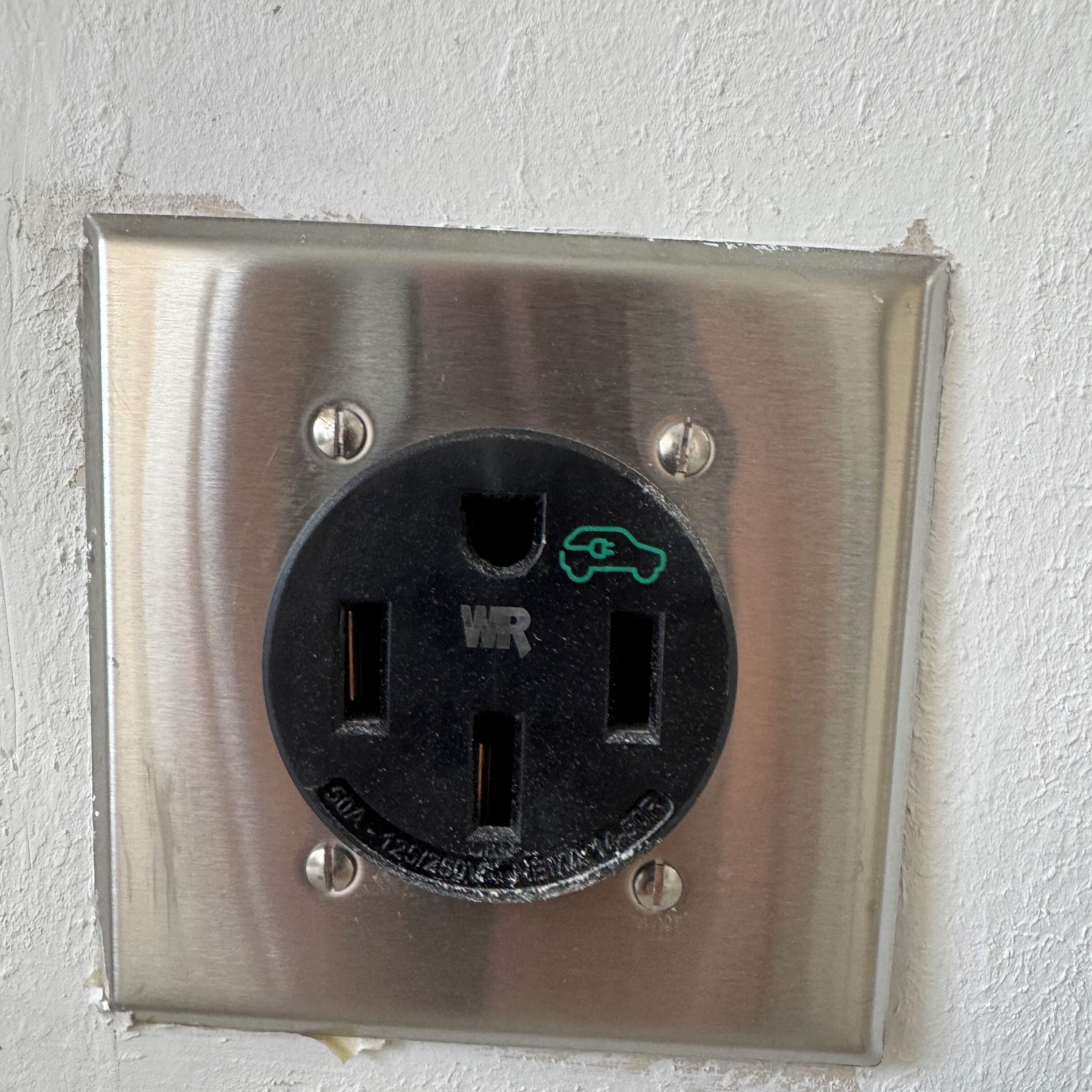 A metallic electrical outlet with a black faceplate, a green plug symbol, and the letters "WR" on it.