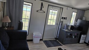 A compact living space with a sofa, a small kitchen area, and a view through the door. - Cozy Cottage With a View in La Grange (La Grange)