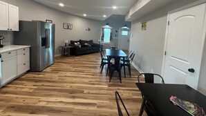 A modern kitchen with stainless steel appliances, a dining area with a black table and chairs, and a cozy living space with a dark sofa.