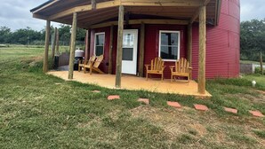 A red cylindrical building with a covered porch and two wooden chairs.