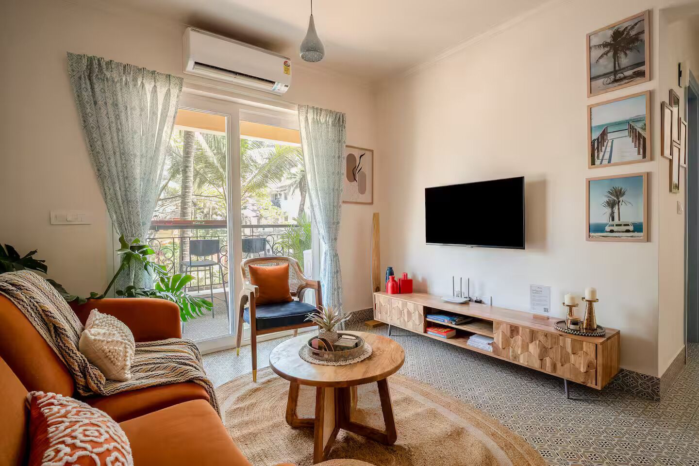 A living room with a sofa, a coffee table, a TV, and a balcony with a view of palm trees.