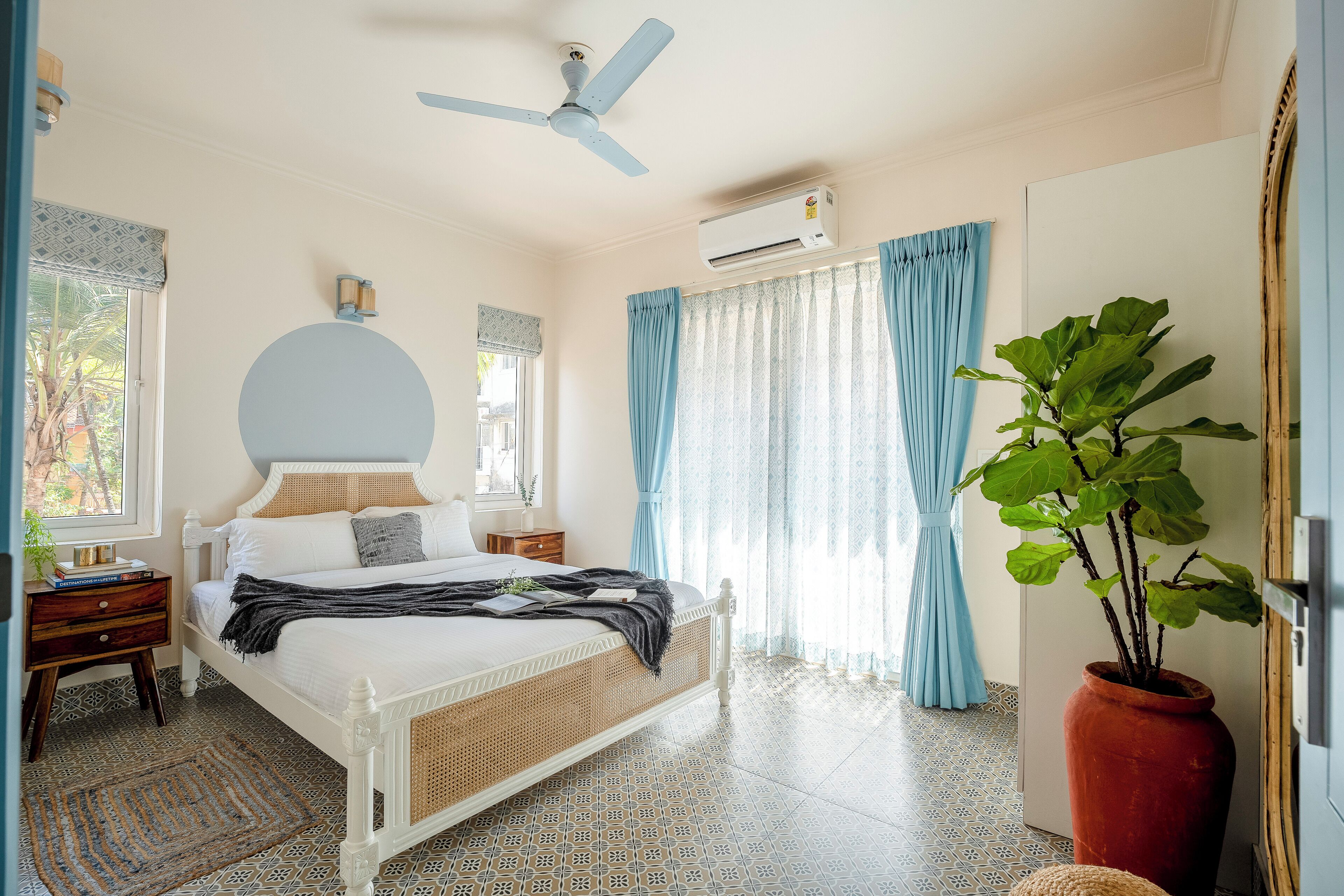 A bedroom with a bed, a ceiling fan, an air conditioner, a potted plant, and a window with curtains.