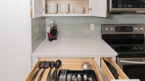 Una cocina con armarios blancos, microondas, horno y un cajón con utensilios.