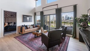 A spacious living room with a large window, a sofa, a coffee table, and a city view. - Skyline Views from Nashville Penthouse – Pool & Minutes to Broadway (Nashville)