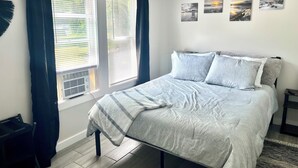 A bedroom with a bed, a window with curtains, a radiator, and wall art.