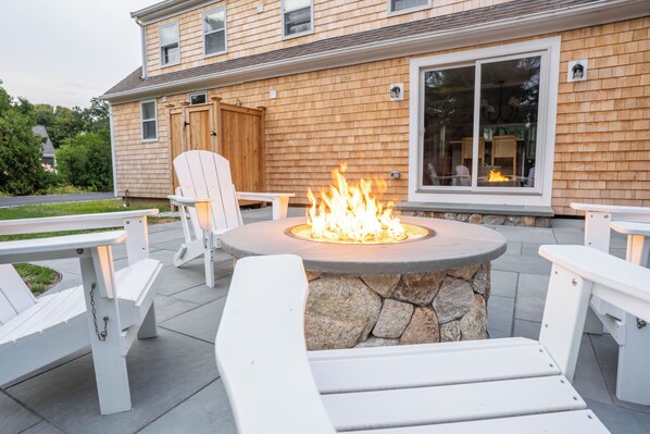 Une terrasse dotée d’un foyer en pierre, entourée de chaises Adirondack blanches.