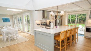 A modern kitchen with a large island, white cabinetry, and a dining area with a white table and chairs. - All-New Coastal Luxury Near CBI & Beaches, Dog-Friendly (Chatham)
