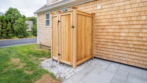 A wooden shed with a metal door, located next to a house with a brick exterior. - All-New Coastal Luxury Near CBI & Beaches, Dog-Friendly (Chatham)