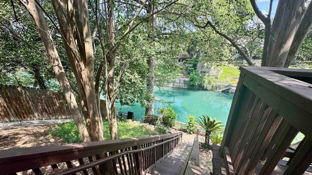 A wooden deck with a view of a lake and surrounding greenery. - Wasser Lodge #102 | Sleeps 5 | Comal Riverfront (New Braunfels)