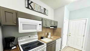 A compact kitchen with a microwave, stove, and sink. There is a coffee maker on the counter, and the kitchen has a 'Kitchen' sign above the microwave. - Wasser Lodge #102 | Sleeps 5 | Comal Riverfront (New Braunfels)