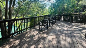 A wooden deck with chairs and a railing overlooking a body of water. - Wasser Lodge #102 | Sleeps 5 | Comal Riverfront (New Braunfels)