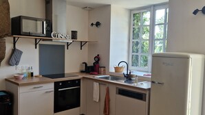 A compact kitchen with a microwave, oven, and refrigerator. There is a window providing natural light and a view of greenery outside. - Gîte du Château de la Haye, I History and Nature (Saint-Hilaire-des-Landes)