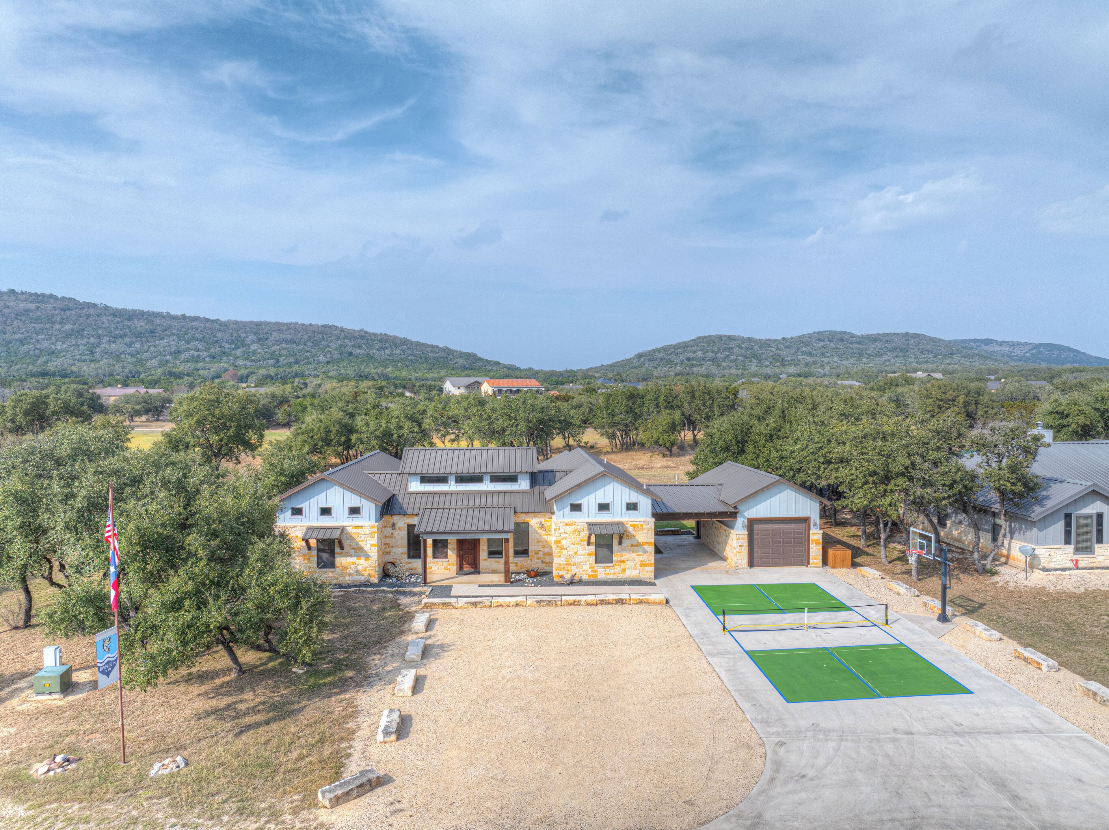 A residential property with a stone facade, a garage, and a tennis court.
