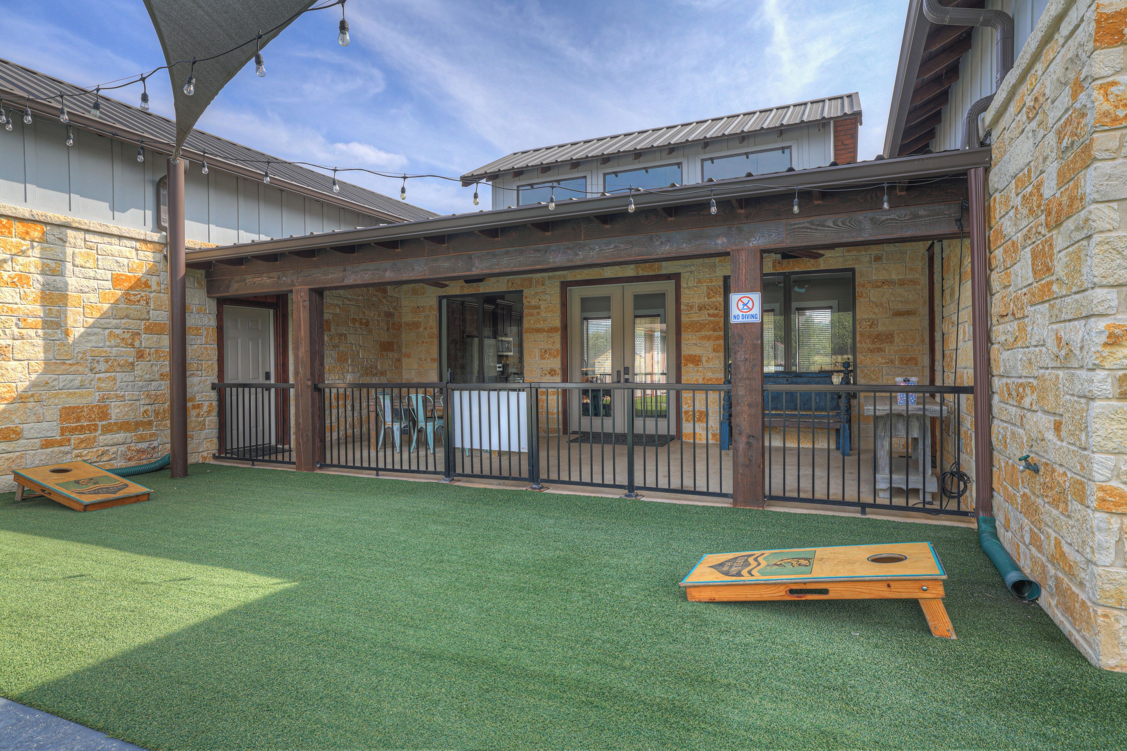 An outdoor patio area with artificial grass, wooden play structures, and a covered seating area with a view of the building's brick facade.